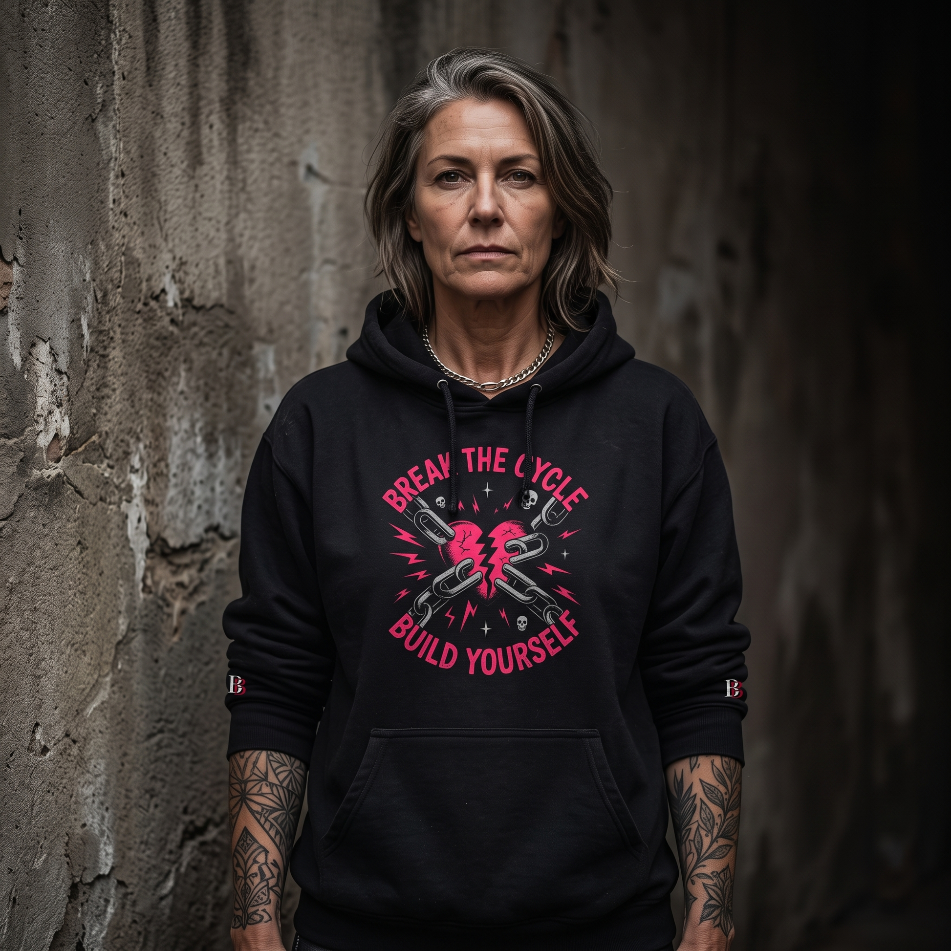 Woomen wearing a Break The Cycle Build Yourself black hoodie with a graphic design and text against a textured wall.