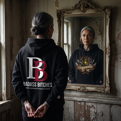 Women wearing a Broken Was The Beginning hoodie with 'Badass Bitches' logo, standing in front of a mirror.