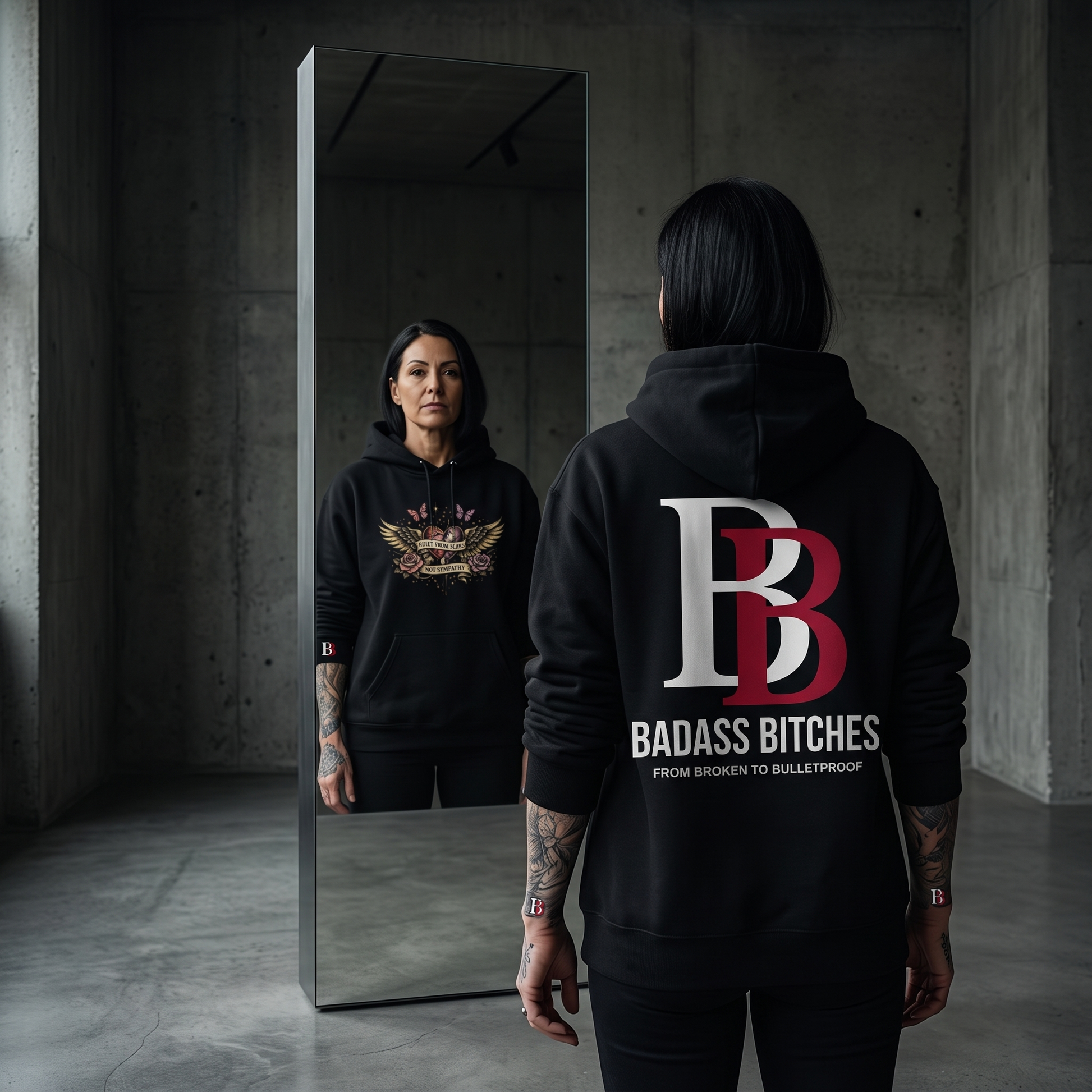 Women wearing a Built From Scars Not Sympathy black hoodie with 'Badass Bitches' logo, standing in a dark room.