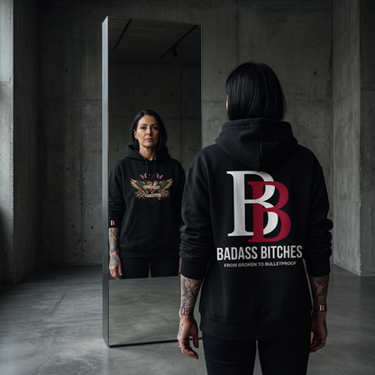 Women wearing a Built From Scars Not Sympathy black hoodie with 'Badass Bitches' logo, standing in a dark room.