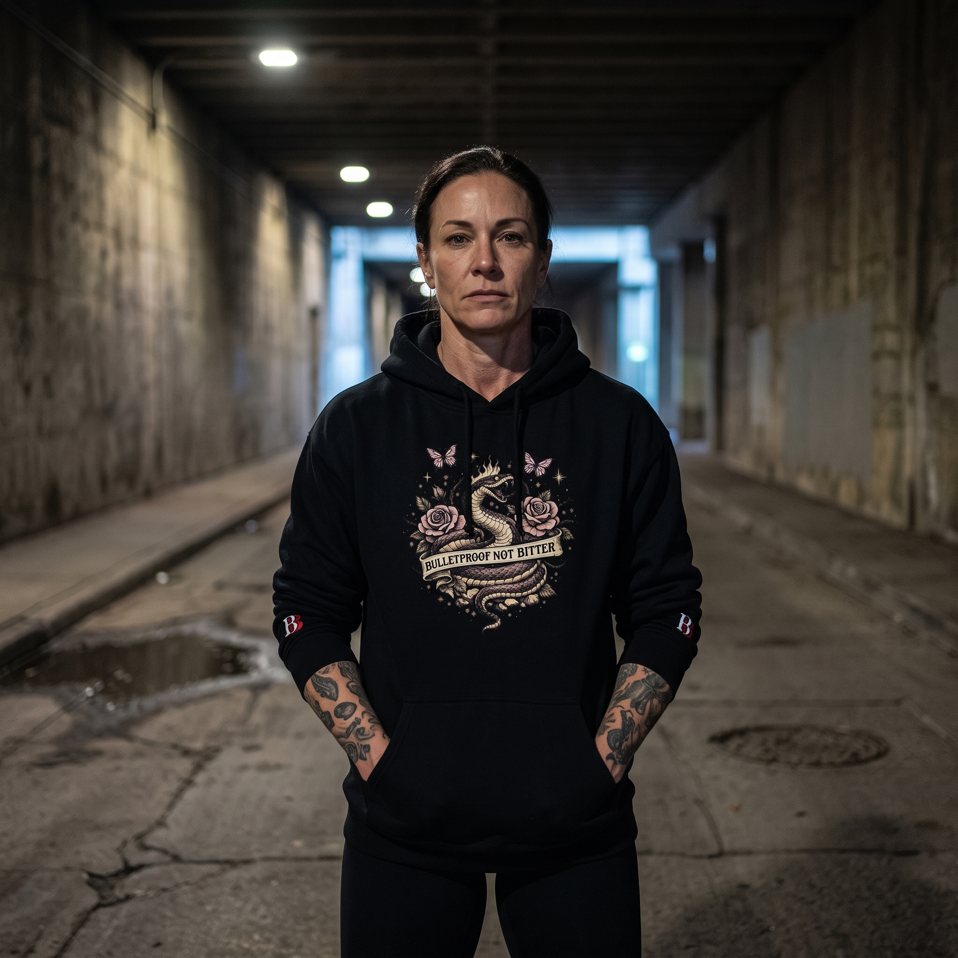 Women wearing a Bulletproof Not Bitter black hoodie with a graphic design in a dimly lit alleyway