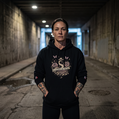 Women wearing a Bulletproof Not Bitter black hoodie with a graphic design in a dimly lit alleyway
