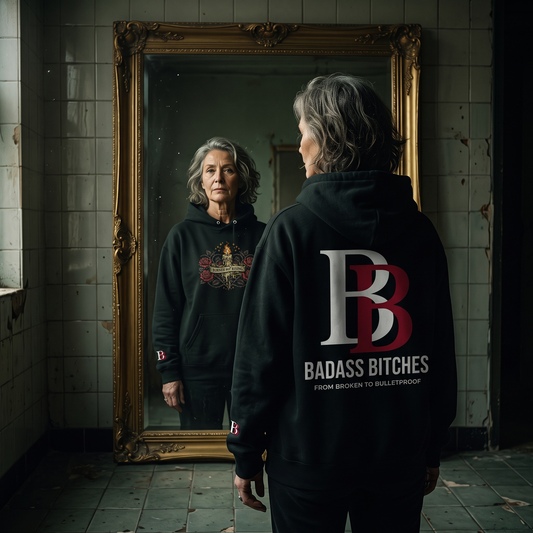 Women  wearing a Burned But Rising hoodie with 'Badass Bitches' logo in a room with a mirror.