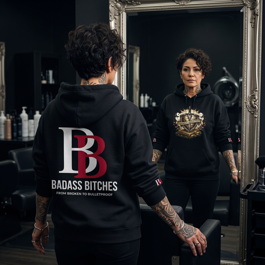 Women wearing a From Broken To Bulletproof black hoodie with Badass Bitches logo, standing in front of a mirror in a salon setting.