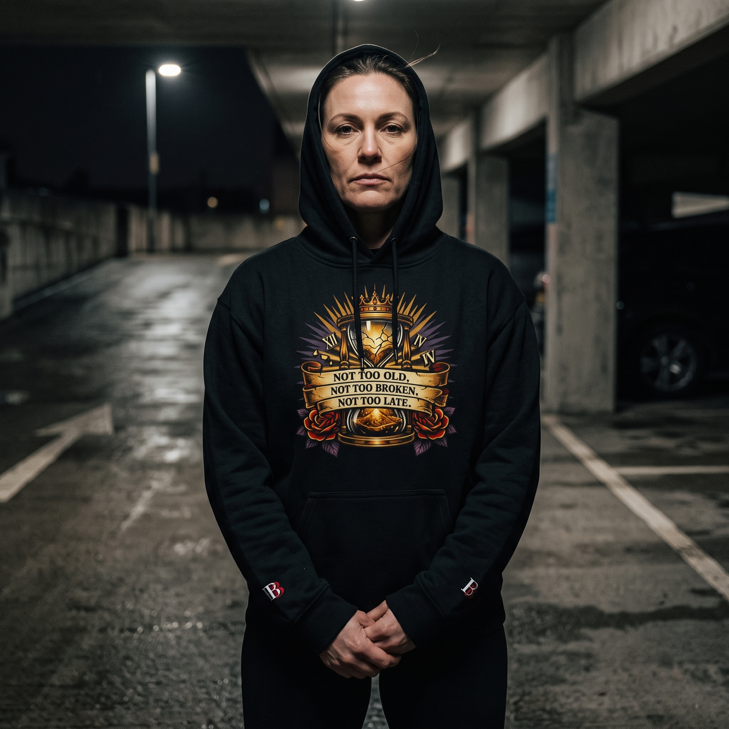 Women wearing a Not Too Old, Not Too Broken, Not Too Late black hoodie with a graphic design in an underground parking lot