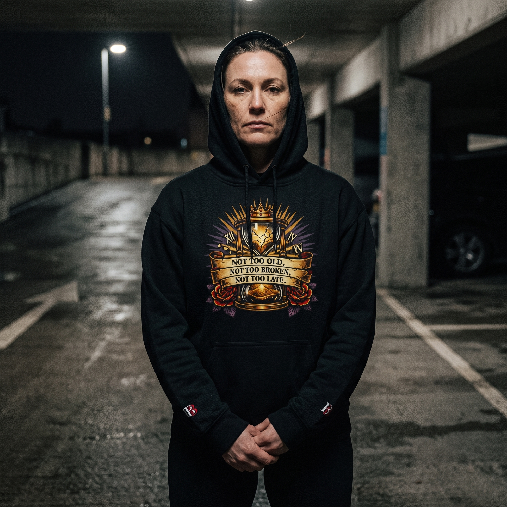 Women wearing a Not Too Old, Not Too Broken, Not Too Late black hoodie with a graphic design in an underground parking lot