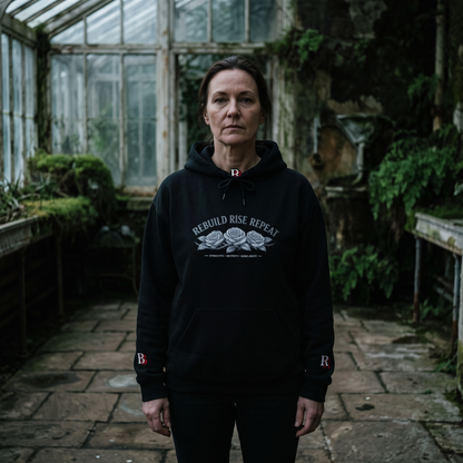 Women wearing a Rebuild Rise Repeat black hoodie with text and roses in a greenhouse