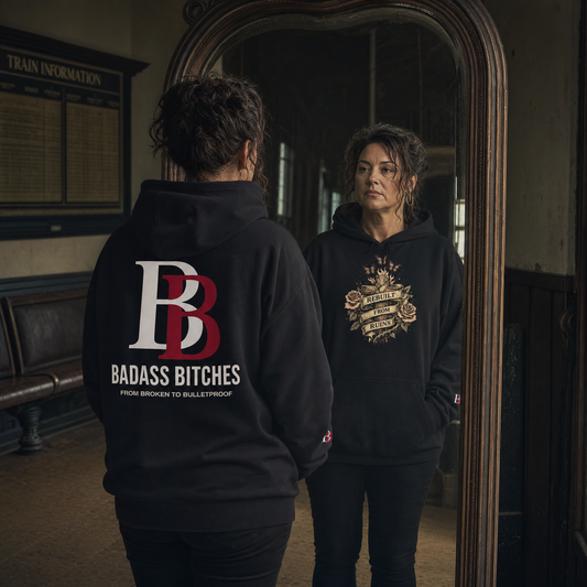Women wearing a Rebuilt From Ruins black hoodie with Badass Bitches logo, standing in front of a mirror.