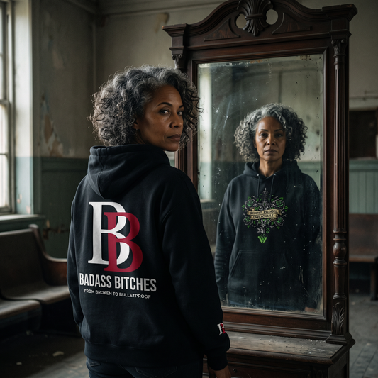Women wearing a Rebuilt Reloaded Unreachable hoodie with Badass Bitches logo standing in front of a mirror in a room.