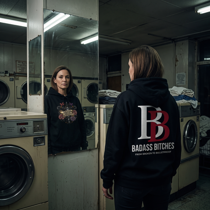 Person wearing a Strength Is Surviving The Days No One Sees hoodie with 'Badass Bitches' text in a laundromat.