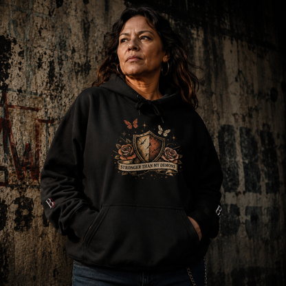 Person wearing a Stronger Than My Demons black hoodie with a graphic design against a textured wall.