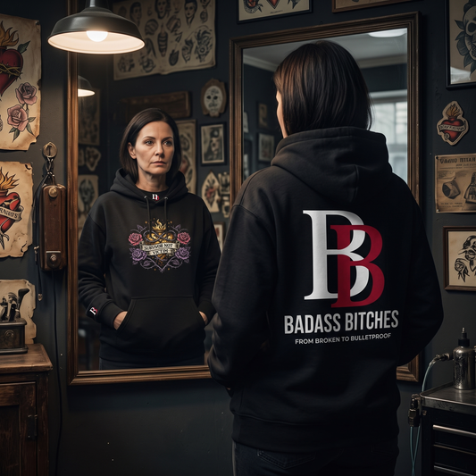 Women wearing a "Survivor Not Victim" black hoodie with 'Badass Bitches' text in a tattoo parlor.