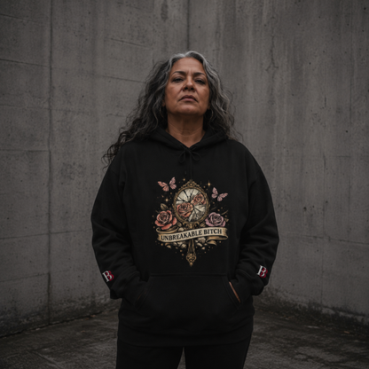 Women wearing a Unbreakable Bitch black hoodie with a graphic design against a gray wall.