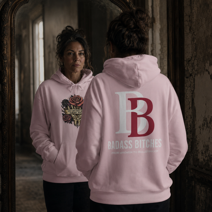 Woman wearing a pink hoodie with a "You can't hurt what's already healed" design on the front and Badass Bitches logo on the back, standing in a dimly lit room.